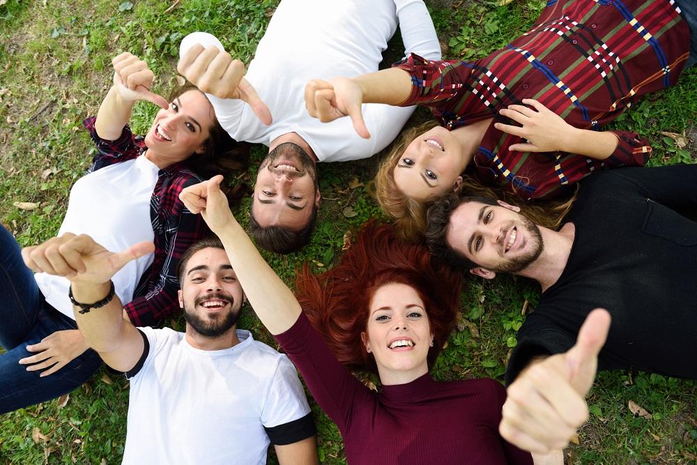 friends-with-thumbs-up-lying-on-the-lawn-of-a-park.jpg